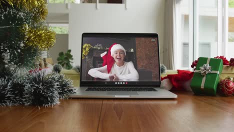 Smiling-caucasian-woman-wearing-santa-hat-on-christmas-video-call-on-laptop