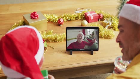Kaukasischer-Vater-Mit-Sohn-Nutzt-Tablet-Für-Weihnachtsvideoanruf-Mit-Lächelndem-Mann-Auf-Dem-Bildschirm