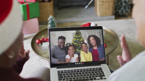 Two-diverse-senior-female-friends-using-laptop-for-christmas-video-call-with-family-on-screen