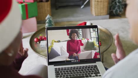 Verschiedene-ältere-Freundinnen-Winken-Und-Benutzen-Laptop-Für-Einen-Weihnachtsvideoanruf-Mit-Einer-Frau-Auf-Dem-Bildschirm