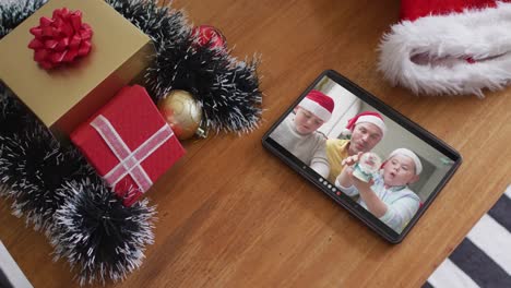 Smiling-caucasian-family-with-santa-hats-on-christmas-video-call-on-tablet