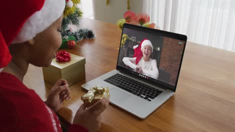 Afroamerikanische-Frau-Mit-Weihnachtsmütze-Nutzt-Laptop-Für-Weihnachtsvideoanruf-Mit-Frau-Auf-Dem-Bildschirm