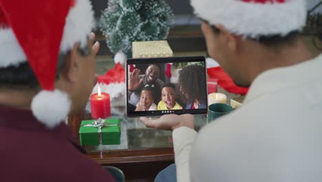 Biracial-father-with-son-waving-and-using-tablet-for-christmas-video-call-with-family-on-screen