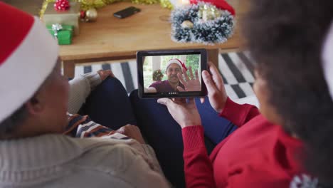 African-american-mother-and-daughter-using-tablet-for-christmas-video-call-with-man-on-screen