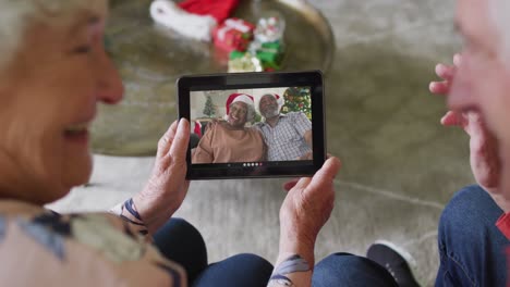 Senior-caucasian-couple-using-tablet-for-christmas-video-call-with-smiling-senior-couple-on-screen
