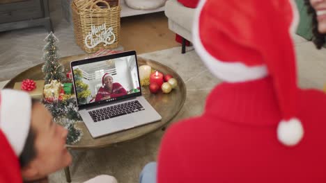African-american-family-with-santa-hats-using-laptop-for-christmas-video-call-with-woman-on-screen
