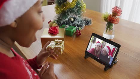 Afroamerikanische-Frau-Mit-Weihnachtsmütze-Nutzt-Tablet-Für-Weihnachtsvideoanruf-Mit-Paar-Auf-Dem-Bildschirm