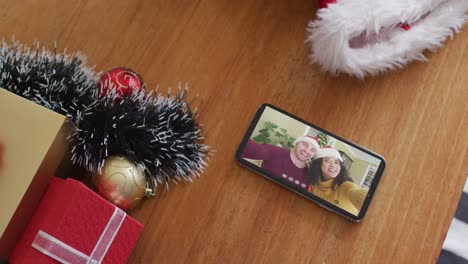 Smiling-diverse-couple-wearing-santa-hats-on-christmas-video-call-on-smartphone