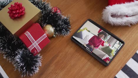 Smiling-african-american-woman-wearing-santa-hat-on-christmas-video-call-on-tablet