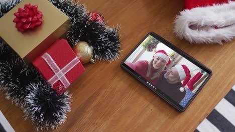 Smiling-caucasian-couple-with-santa-hats-on-christmas-video-call-on-tablet