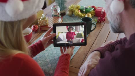Kaukasisches-Paar-Mit-Weihnachtsmützen-Nutzt-Tablet-Für-Weihnachtsvideoanruf-Mit-Lächelndem-Freund-Auf-Dem-Bildschirm