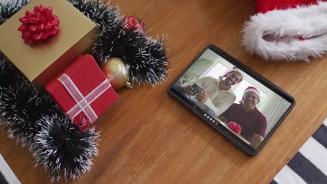 Smiling-biracial-father-and-son-wearing-santa-hats-on-christmas-video-call-on-tablet