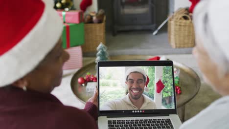 Zwei-Verschiedene-ältere-Freundinnen-Nutzen-Ihren-Laptop-Für-Einen-Weihnachtsvideoanruf-Mit-Einem-Mann-Auf-Dem-Bildschirm