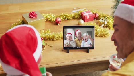 Kaukasischer-Vater-Und-Sohn-Mit-Weihnachtsmützen-Nutzen-Tablet-Für-Weihnachtsvideoanruf-Mit-Der-Familie-Auf-Dem-Bildschirm