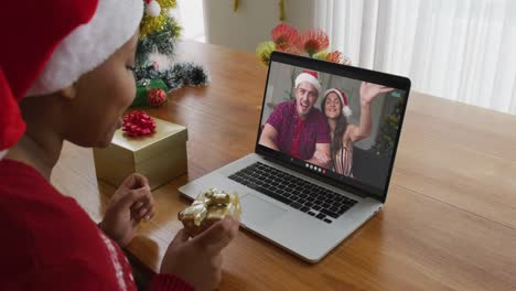 African-american-woman-with-santa-hat-using-laptop-for-christmas-video-call-with-couple-on-screen
