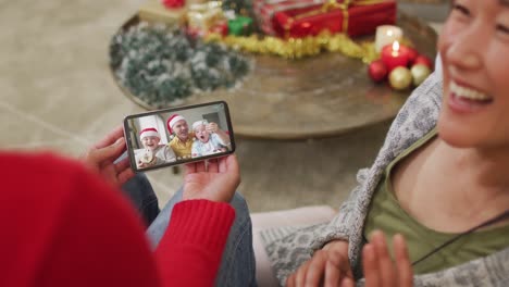 Smiling-asian-couple-using-smartphone-for-christmas-video-call-with-family-with-santa-hats-on-screen
