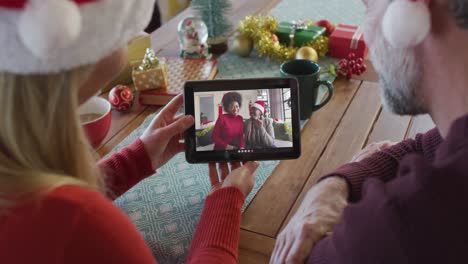 Caucasian-couple-with-santa-hats-using-tablet-for-christmas-video-call-with-smiling-family-on-screen