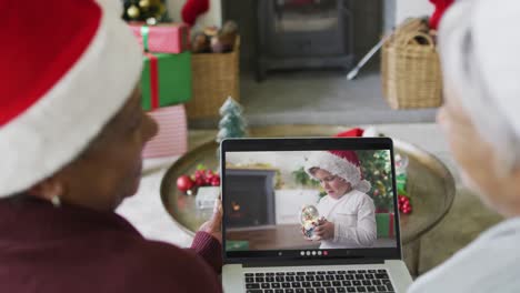 Two-diverse-senior-female-friends-using-laptop-for-christmas-video-call-with-boy-on-screen