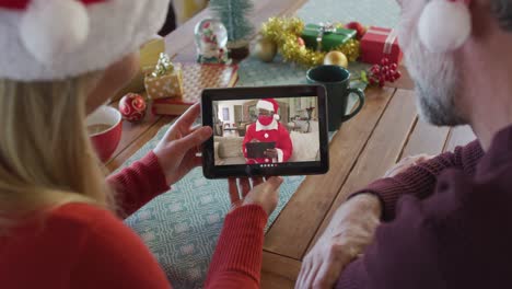 Kaukasisches-Paar-Mit-Weihnachtsmützen-Nutzt-Tablet-Für-Weihnachtsvideoanruf-Mit-Weihnachtsmann-Auf-Dem-Bildschirm