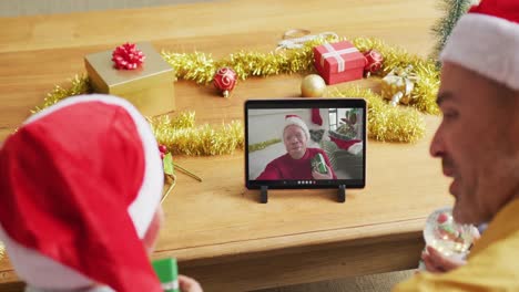 Caucasian-father-and-son-with-santa-hats-using-tablet-for-christmas-video-call-with-man-on-screen