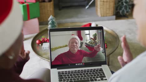 Diverse-senior-female-friends-waving-and-using-laptop-for-christmas-video-call-with-man-on-screen