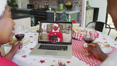 Lächelndes-Afroamerikanisches-Paar,-Das-Einen-Laptop-Für-Einen-Weihnachtsvideoanruf-Mit-Dem-Weihnachtsmann-Auf-Dem-Bildschirm-Benutzt