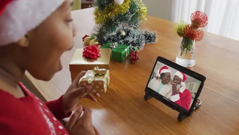 Afroamerikanische-Frau-Mit-Weihnachtsmütze-Nutzt-Tablet-Für-Weihnachtsvideoanruf-Mit-Paar-Auf-Dem-Bildschirm