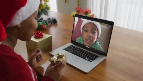 Mujer-Afroamericana-Con-Sombrero-De-Santa-Usando-Una-Computadora-Portátil-Para-Una-Videollamada-Navideña-Con-Un-Niño-En-La-Pantalla