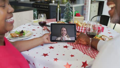 African-american-couple-with-wine-using-tablet-for-christmas-video-call-with-happy-woman-on-screen
