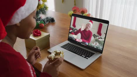 Afroamerikanische-Frau-Mit-Weihnachtsmütze-Nutzt-Laptop-Für-Weihnachtsvideoanruf-Mit-Mann-Auf-Dem-Bildschirm