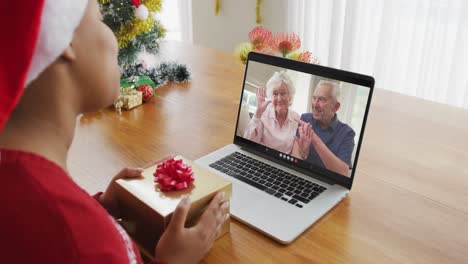 African-american-woman-using-laptop-for-christmas-video-call-with-smiling-senior-couple-on-screen