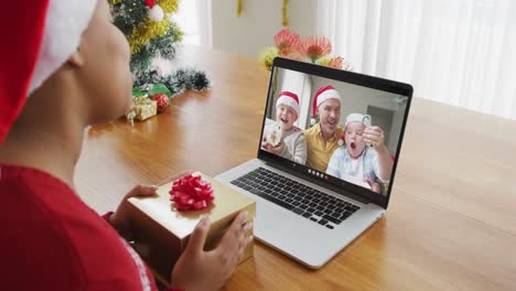 African-american-woman-with-santa-hat-using-laptop-for-christmas-video-call,-with-family-on-screen