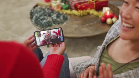 Smiling-asian-couple-using-smartphone-for-christmas-video-call-with-caucasian-couple-on-screen