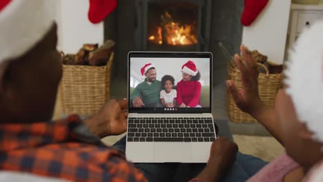 Afroamerikanisches-Paar-Mit-Weihnachtsmützen-Nutzt-Laptop-Für-Weihnachtsvideoanruf-Mit-Der-Familie-Auf-Dem-Bildschirm