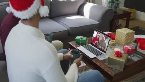 Biracial-father-and-son-with-santa-hats-using-laptop-for-christmas-video-call-with-family-on-screen