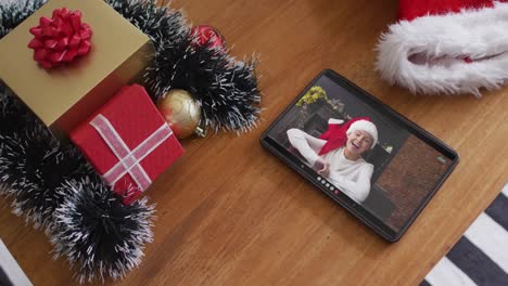 Smiling-caucasian-woman-wearing-santa-hat-on-christmas-video-call-on-tablet