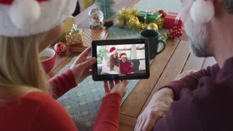 Kaukasisches-Paar-Mit-Weihnachtsmützen-Nutzt-Tablet-Für-Weihnachtsvideoanruf-Mit-Der-Familie-Auf-Dem-Bildschirm