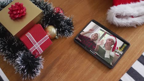 Smiling-caucasian-father-and-son-wearing-santa-hats-on-christmas-video-call-on-tablet