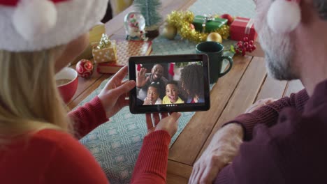 Lächelndes-Kaukasisches-Paar-Mit-Weihnachtsmützen,-Das-Ein-Tablet-Für-Einen-Weihnachtsvideoanruf-Mit-Der-Familie-Auf-Dem-Bildschirm-Nutzt