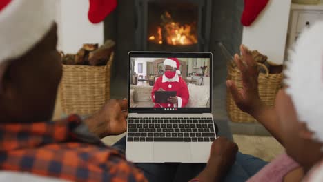 African-american-couple-using-laptop-for-christmas-video-call-with-santa-on-screen