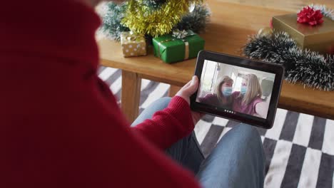 Caucasian-man-waving-and-using-tablet-for-christmas-video-call-with-smiling-family-on-screen
