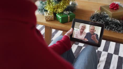 Caucasian-man-waving-and-using-tablet-for-christmas-video-call-with-smiling-couple-on-screen