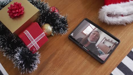 Lächelnde-Kaukasische-Frau-Mit-Gesichtsmaske-Bei-Weihnachtsvideoanruf-Auf-Dem-Tablet