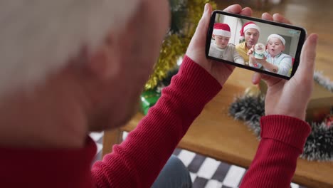 Kaukasischer-Mann-Mit-Weihnachtsmütze-Nutzt-Smartphone-Für-Weihnachtsvideoanruf-Mit-Lächelnder-Familie-Auf-Dem-Bildschirm