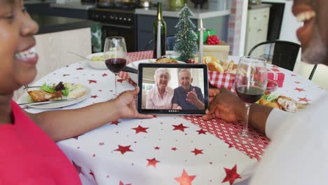 Smiling-african-american-couple-using-tablet-for-christmas-video-call-with-happy-couple-on-screen