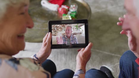 Senior-caucasian-couple-smiling-and-using-tablet-for-christmas-video-call-with-man-on-screen