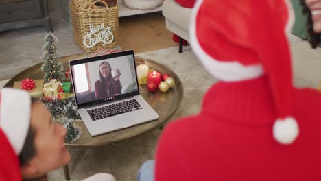Diverse-family-with-santa-hats-using-laptop-for-christmas-video-call-with-happy-woman-on-screen
