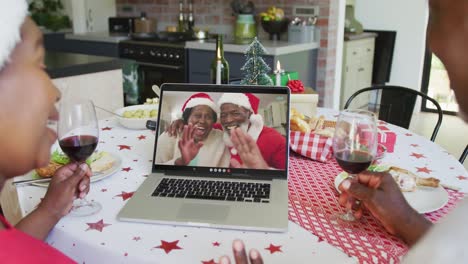 African-american-couple-with-wine-using-laptop-for-christmas-video-call-with-happy-couple-on-screen