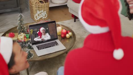 Eine-Vielfältige-Familie-Mit-Weihnachtsmützen-Nutzt-Laptop-Für-Einen-Weihnachtsvideoanruf-Mit-Einer-Glücklichen-Frau-Auf-Dem-Bildschirm