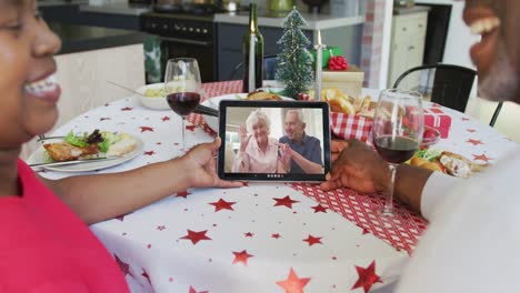 Smiling-african-american-couple-using-tablet-for-christmas-video-call-with-happy-couple-on-screen